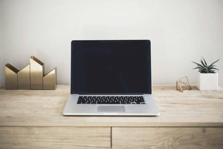 Laptop op een houten bureau bij een lichte muur